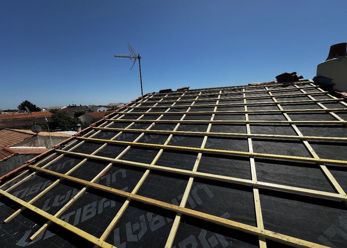 Liteaux et contre-liteaux posés en quadrillage sur un écran sous-toiture, sous un ciel bleu